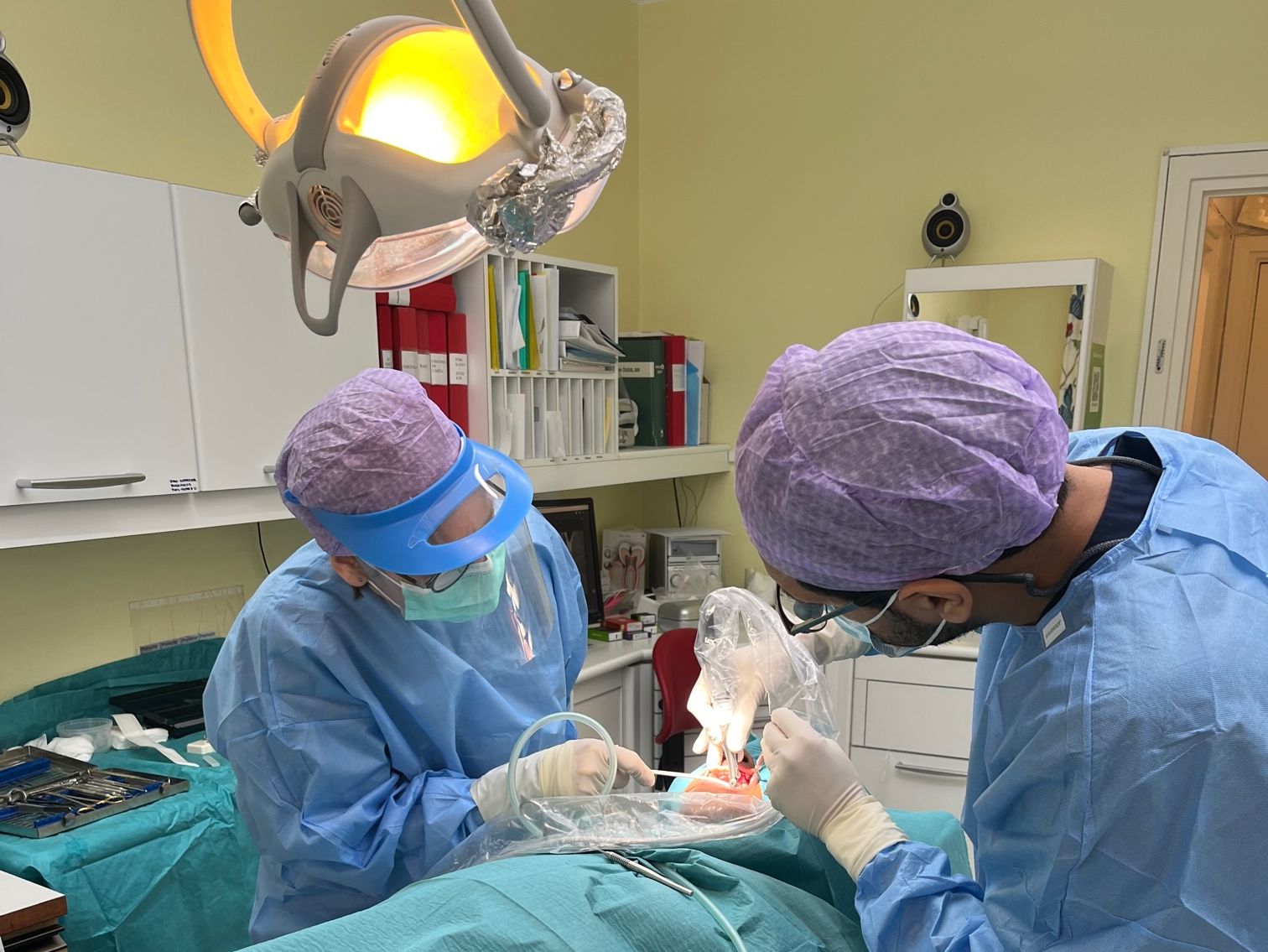 Två personer i lila hårskydd, blå kläder som undersöker en patient i munnen